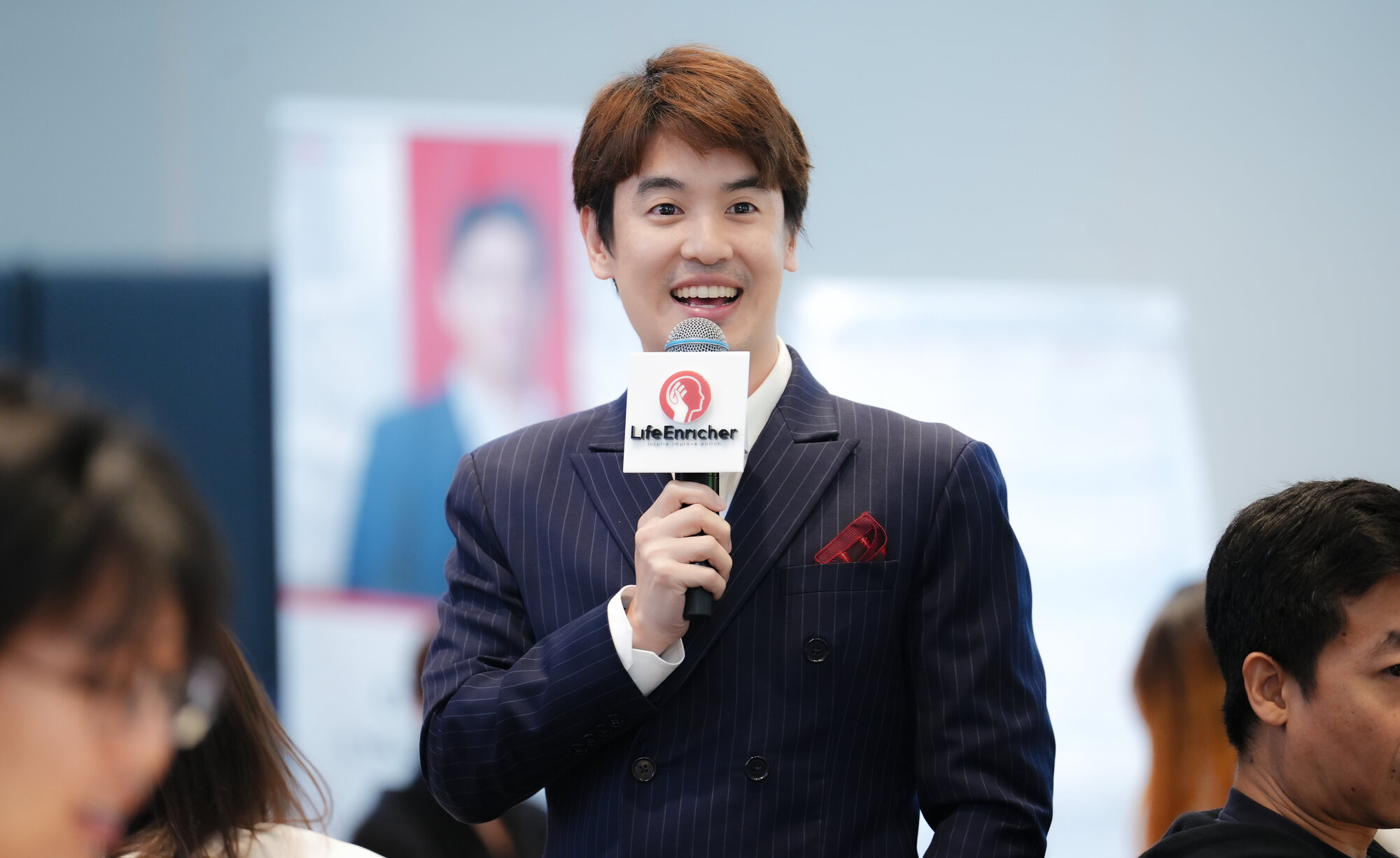 โอม OMEHARIN ถือไมโครโฟน ยิ้มในห้องสัมมนา
